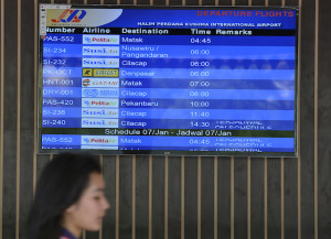 Calon penumpang melintas di depan layar monitor informasi keberangkatan di Bandara Halim Perdanakusuma, Jakarta, Senin (6/1).